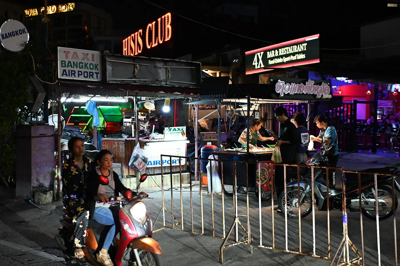 A busy Pattaya street at night with motorbikes passing food stalls